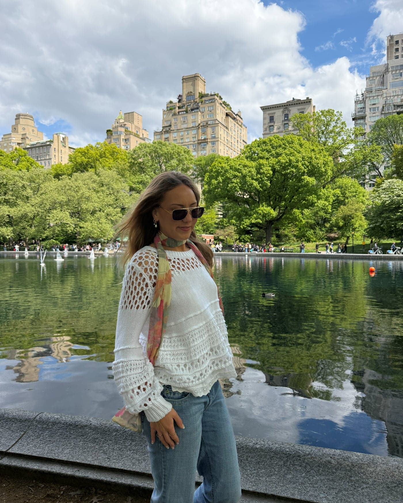 Lauren Peyton in a white crochet knit and silk scarf beside the Conservatory Water in Central Park